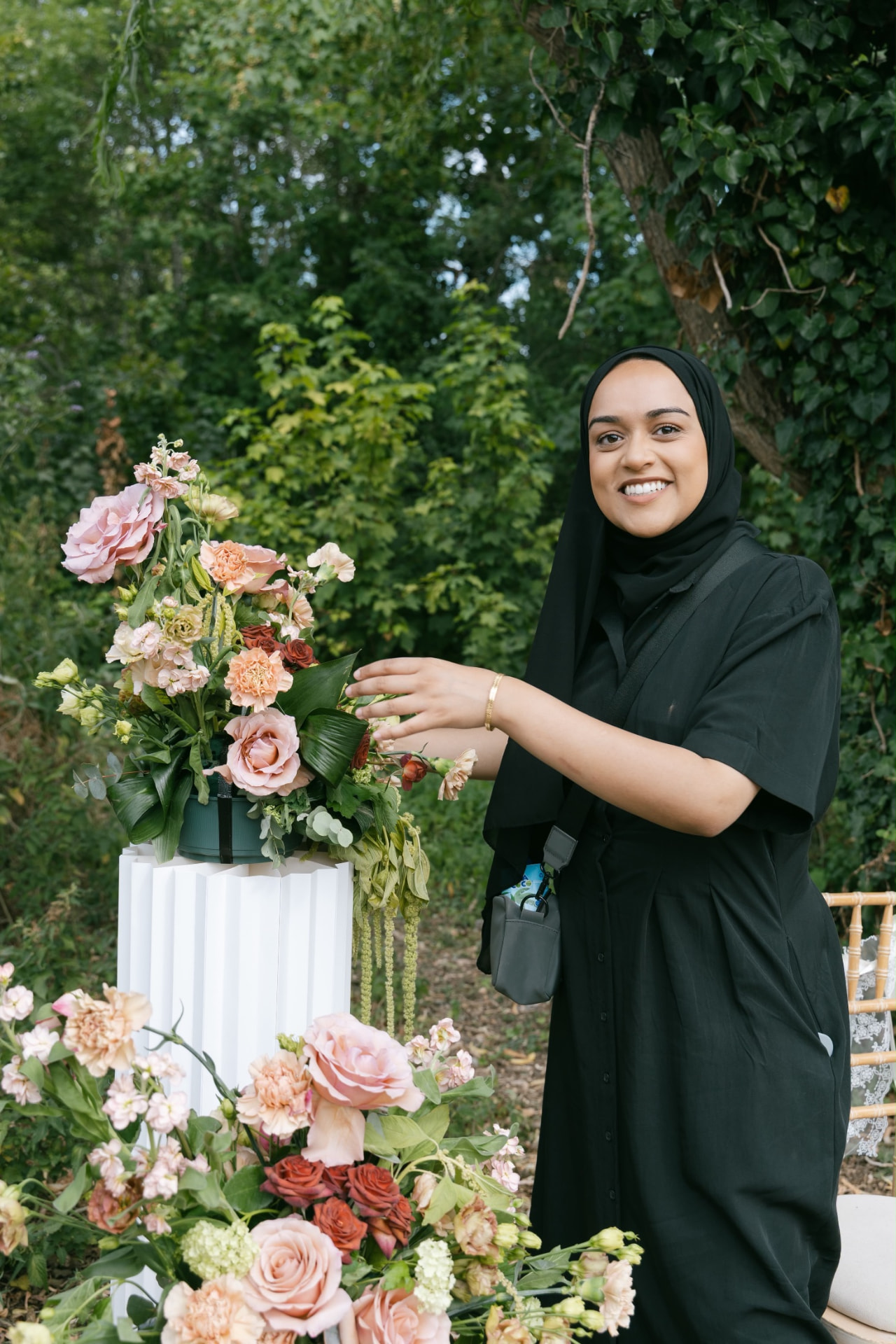 Fahima arranging a blush and peach floral display in a garden before guests arrive