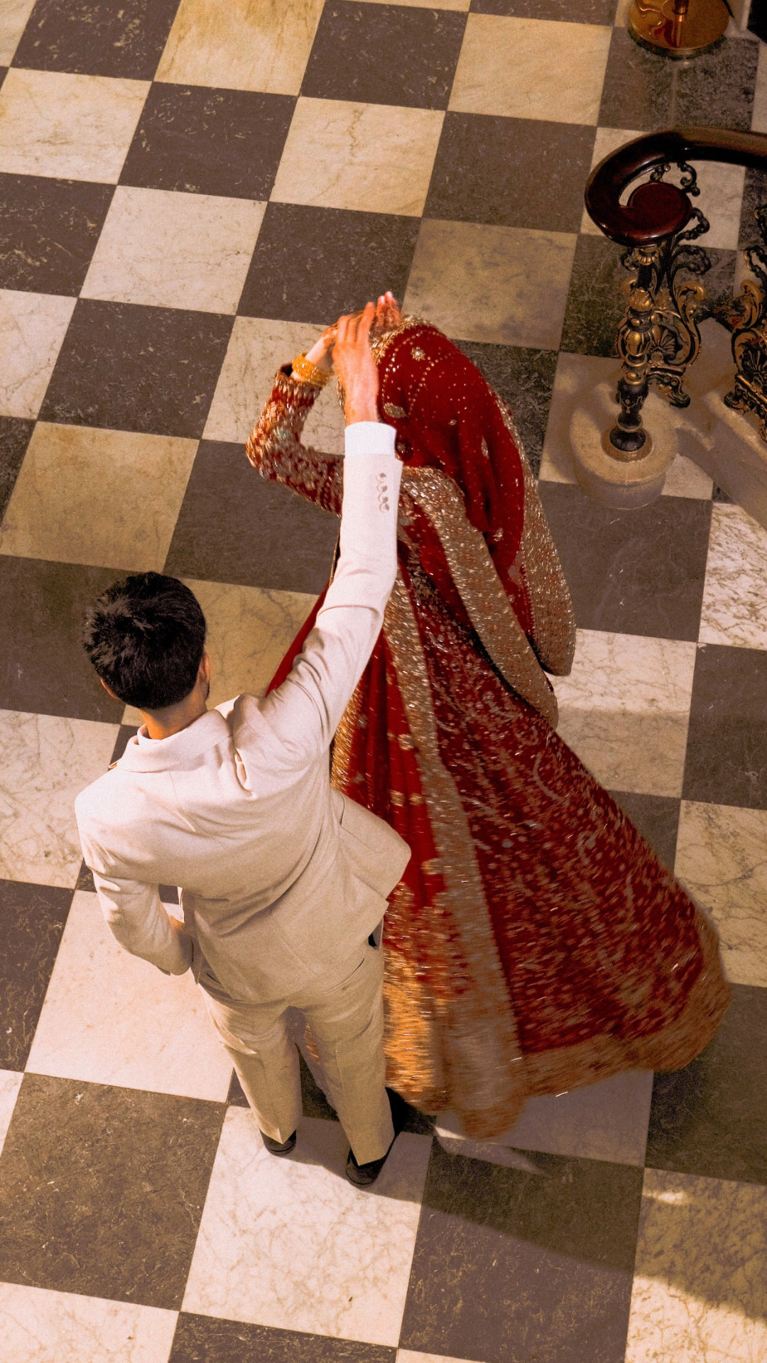 Groom leading the bride across a chequered marble floor, her red lengha sweeping behind her