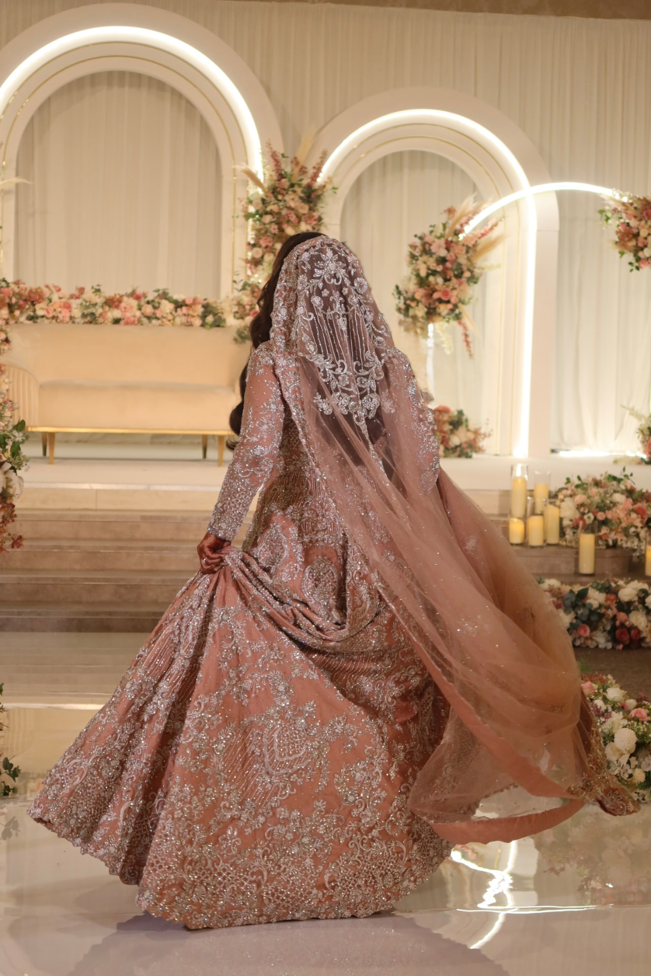 Bride in a blush embroidered gown turning in front of an arched floral stage