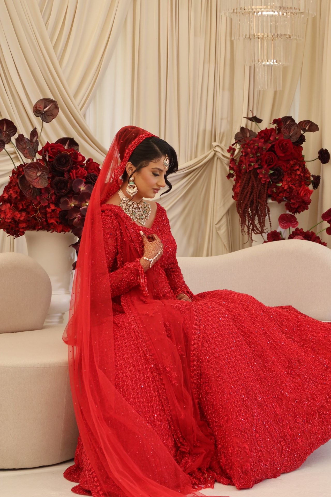 Bride in red seated in front of deep red florals and cream drapes