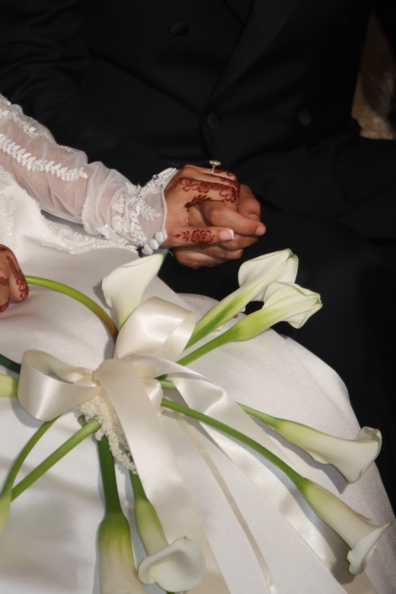 Bride and groom holding hands over a calla lily bouquet, henna on the bride's hands